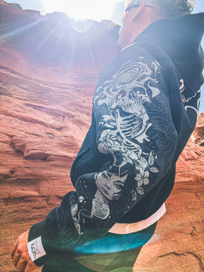 Person wearing a black jacket with white designs against a rocky background