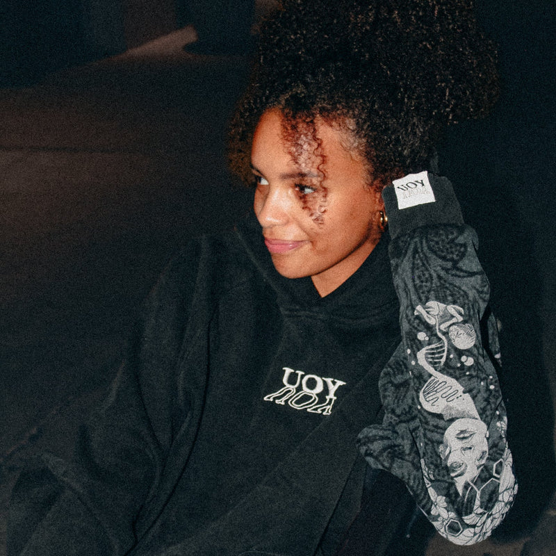 Person wearing a black hoodie with YOU branding, sitting on a dark surface.