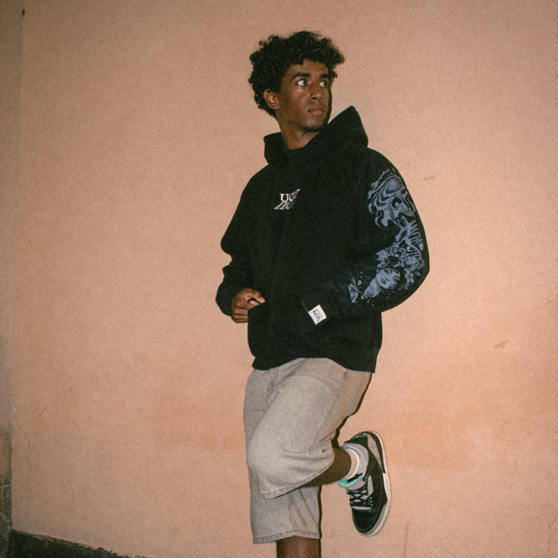 Person wearing a YOU hoodie against a pink wall.