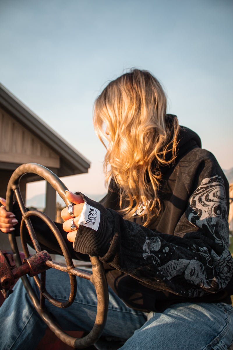 Person sitting on a rustic vehicle with a steering wheel, wearing a YOU hoodie with a graphic design.