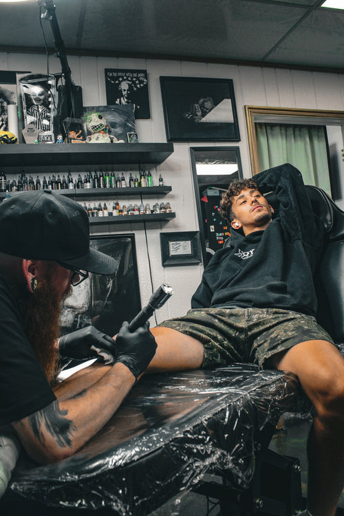 Tattoo artist at work in a tattoo parlor with a client receiving a tattoo.